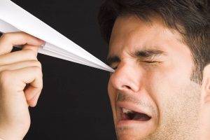 man poking eye with paper airplane